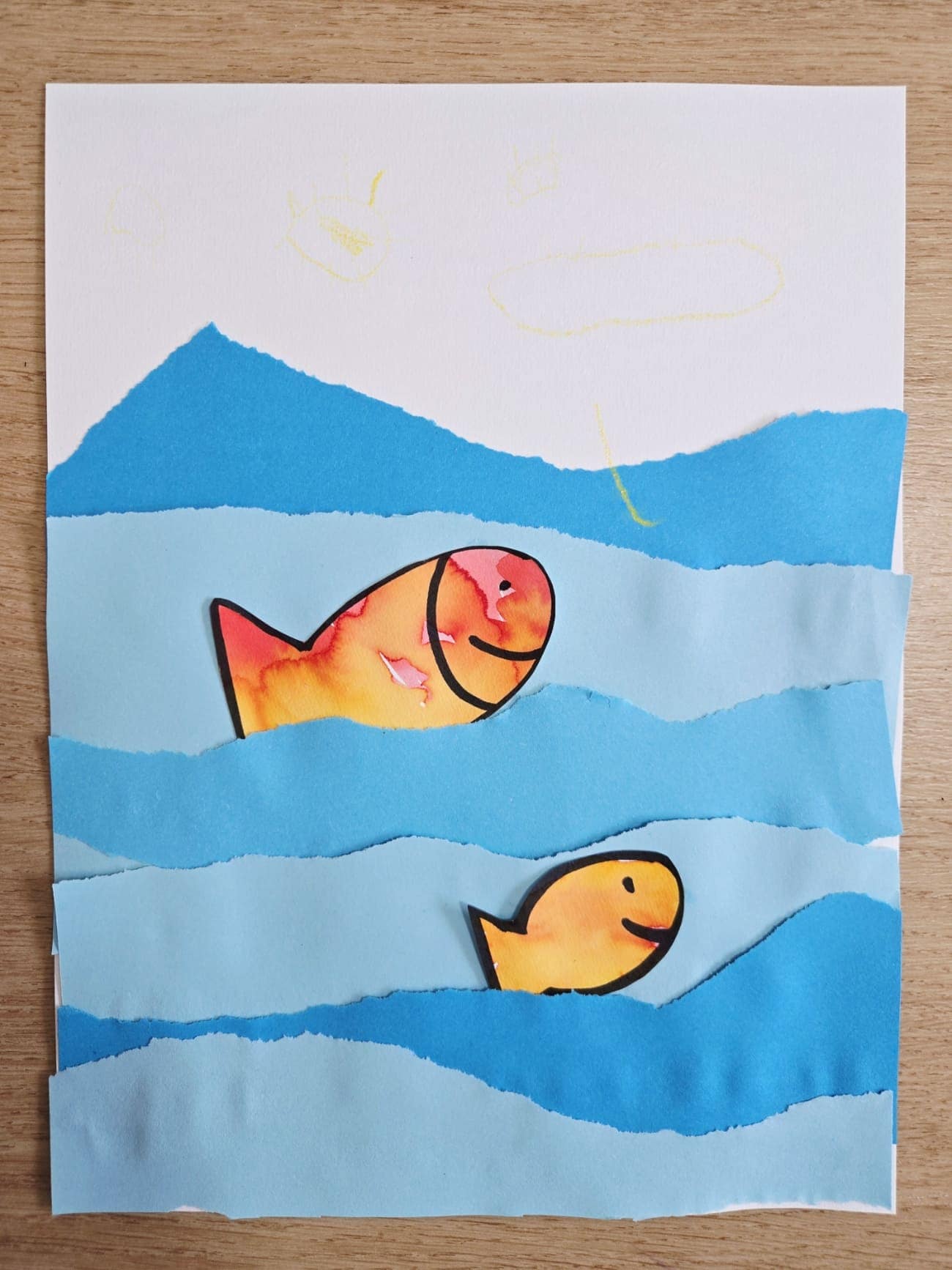 Activité réalisée par un enfant de 3 ans : collage de poissons peints à l’encre dans une mer en papier bleu