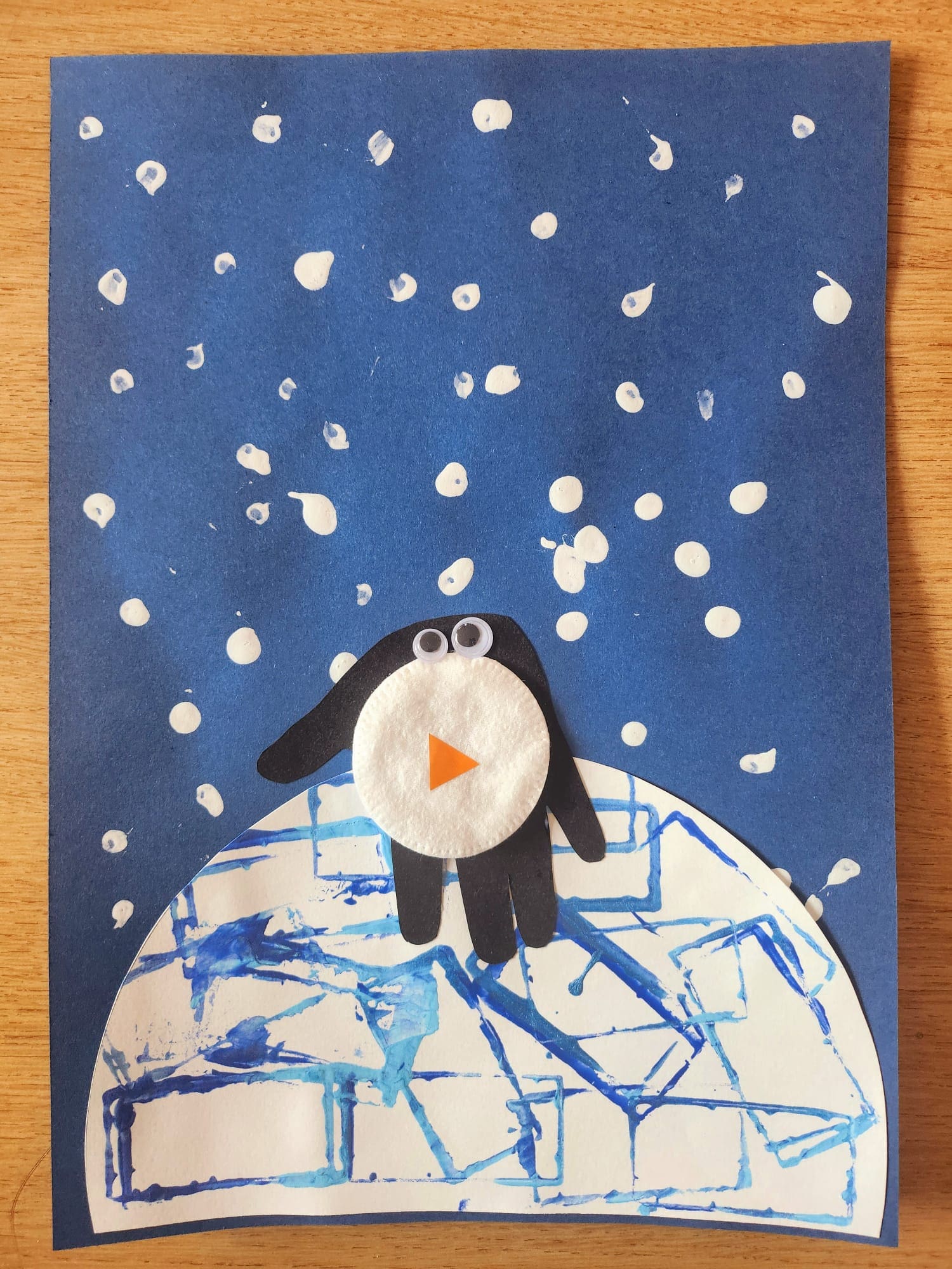 Activité manuelle pour enfants : pingouin sur un igloo avec un fond enneigé, réalisée avec peinture et tampons.