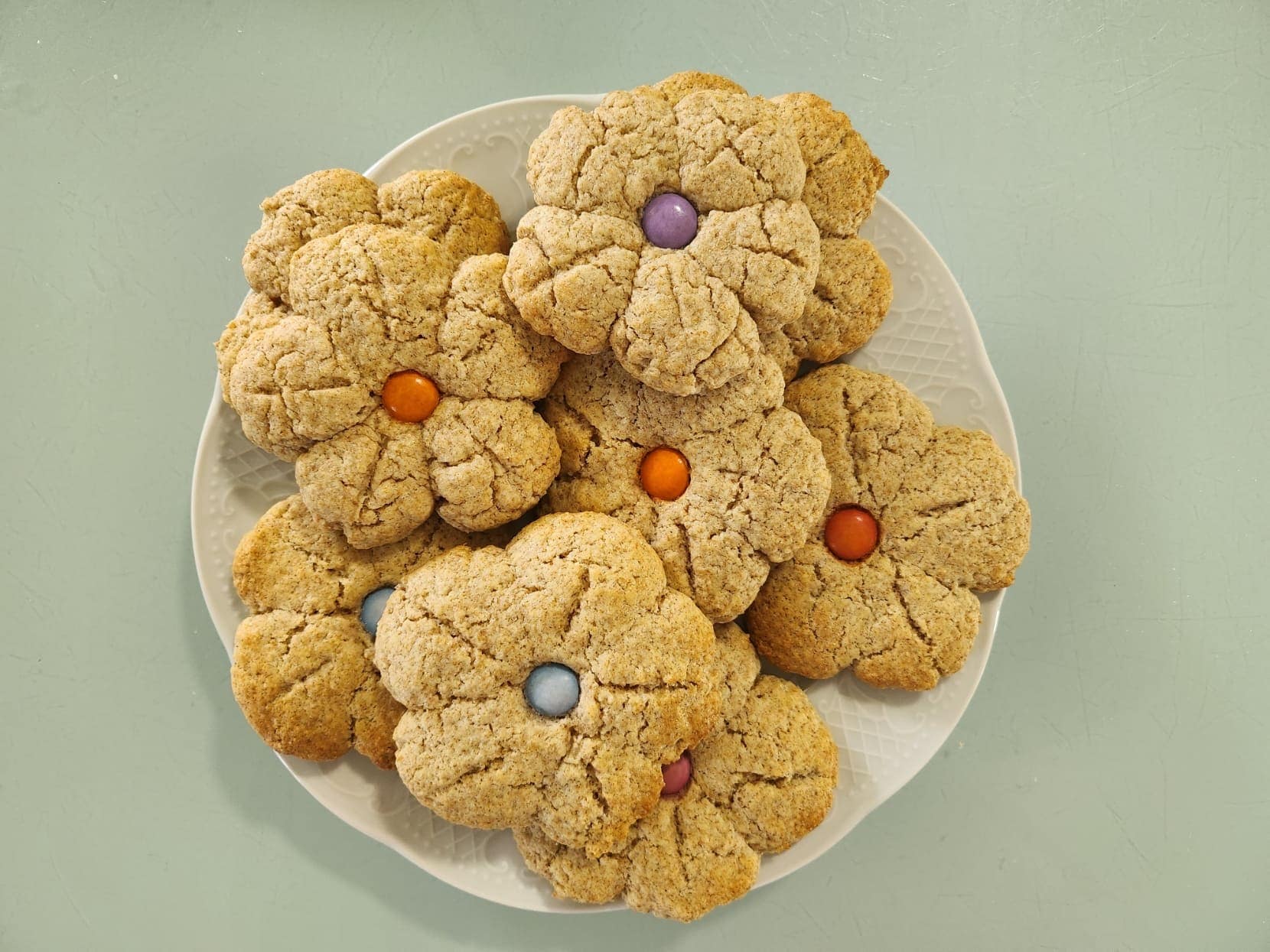 Assiette de cookies maison en forme de fleurs, décorés de bonbons colorés au centre.
