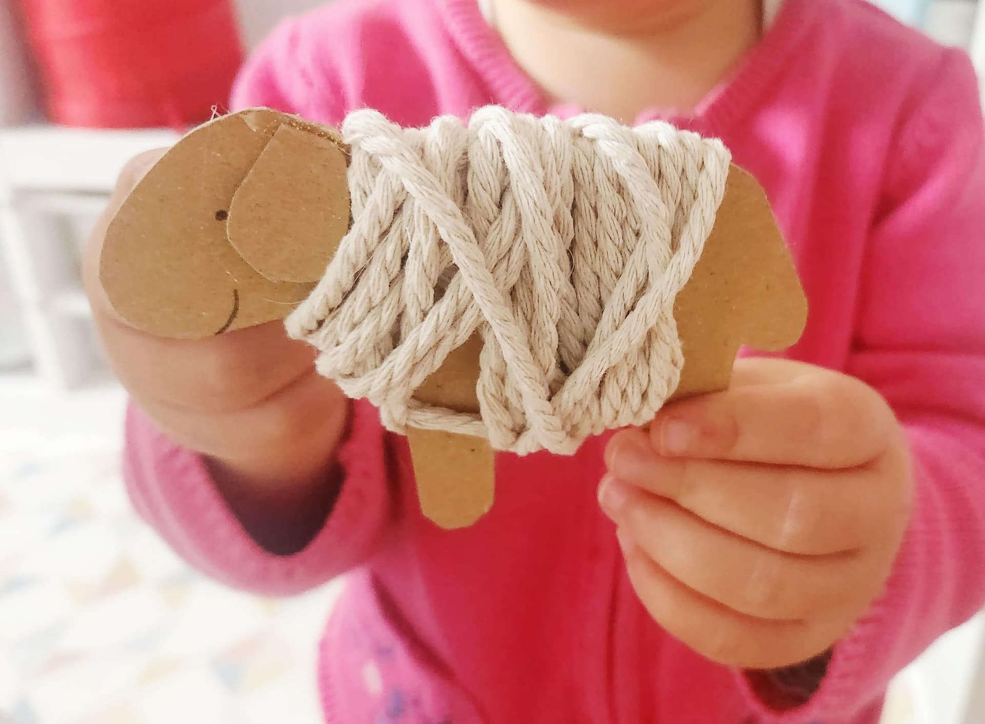 Enfant montrant fièrement un mouton en carton recouvert de laine blanche, bricolage terminé.