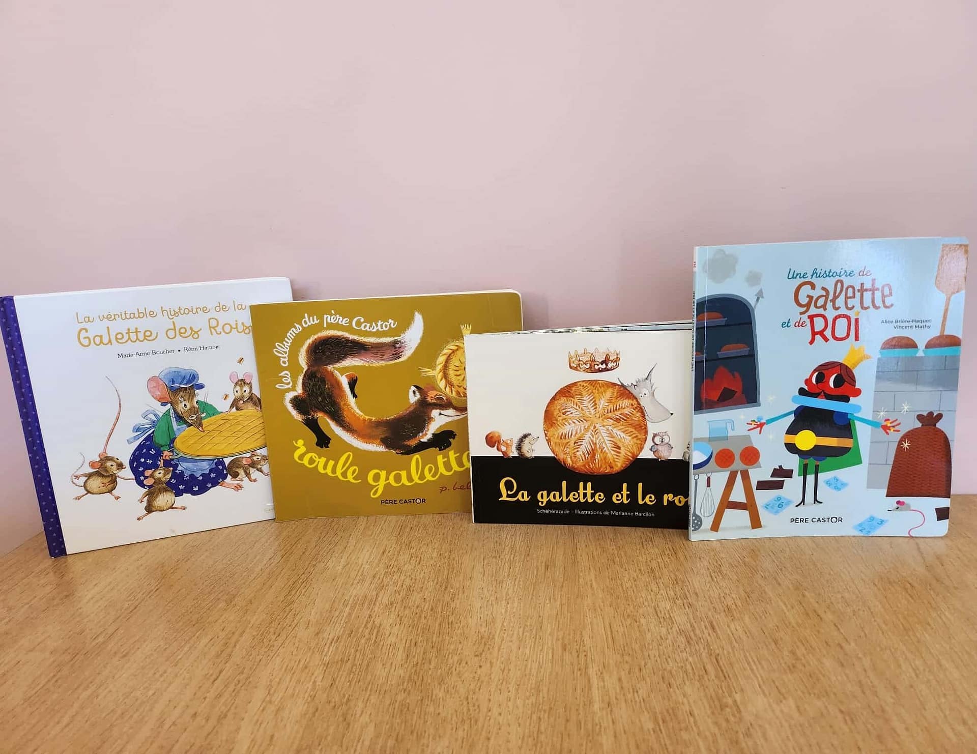 Quatre livres pour enfants sur la Galette des Rois, disposés sur une table en bois avec un fond rose.