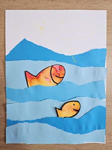 Activité réalisée par un enfant de 3 ans : collage de poissons peints à l’encre dans une mer en papier bleu