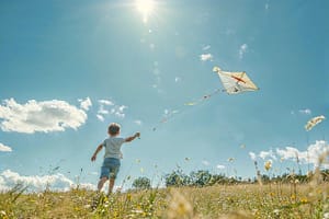 Regarder le monde à travers les yeux d'un enfant. Un jeune garçon en t-shirt blanc et short bleu fait voler un cerf-volant dans un champ ensoleillé, reflétant la simplicité et la joie de l’enfance.