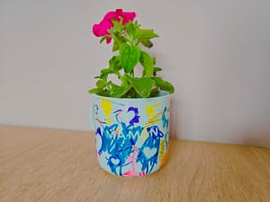 Mug décoré par un enfant avec des dessins colorés, utilisé comme pot de fleurs pour un cadeau de fête des mères.