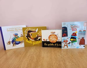 Quatre livres pour enfants sur la Galette des Rois, disposés sur une table en bois avec un fond rose.
