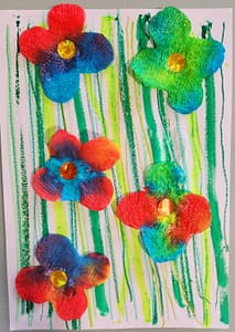 Résultat final de l’activité : fleurs en papier absorbant colorées, décorées de strass, collées sur un fond aux lignes vertes.