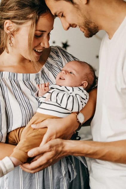 Jeune couple tenant un nouveau-né dans leurs bras, image illustrant la parentalité et le lien familial.