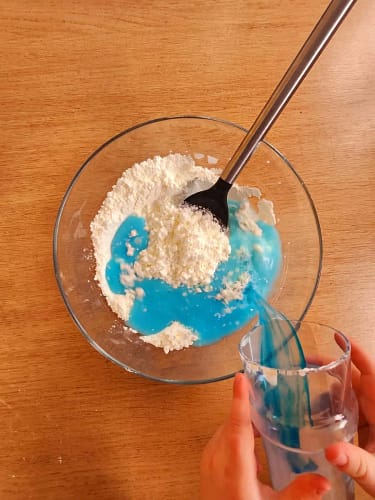 Versement d’eau colorée sur de la maïzena dans un bol, étape de préparation de l’oobleck, un fluide non newtonien.