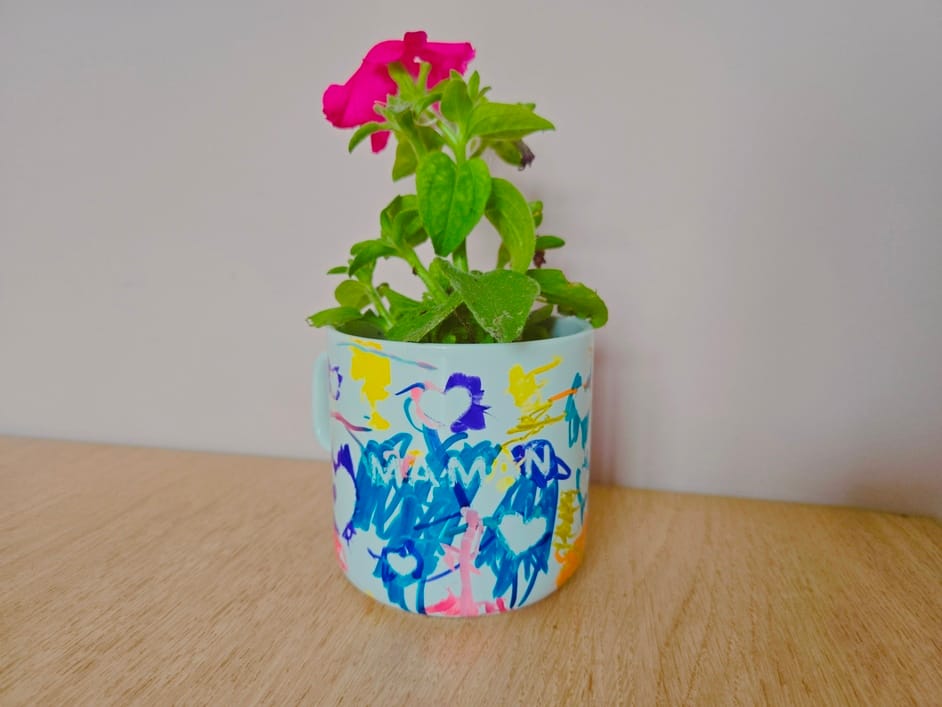 Mug décoré par un enfant avec des dessins colorés, utilisé comme pot de fleurs pour un cadeau de fête des mères.
